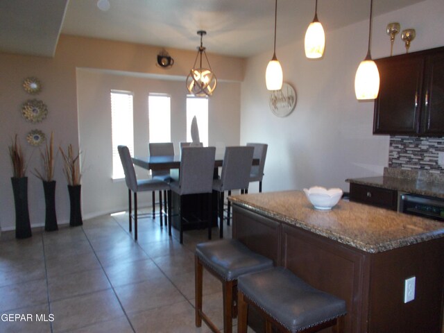 kitchen featuring pendant lighting, dark brown cabinets, tile patterned flooring, dark stone counters, and decorative backsplash