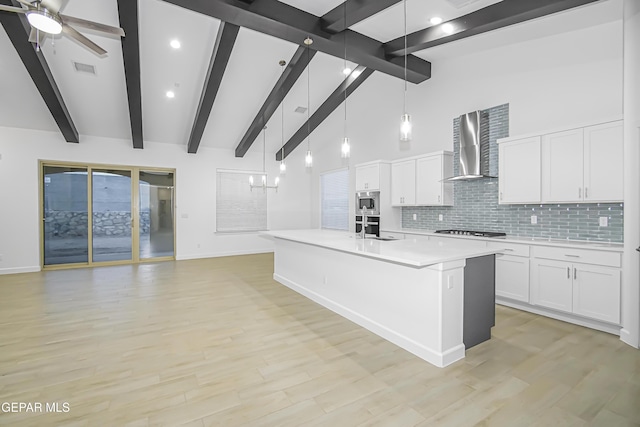 kitchen featuring white cabinetry, wall chimney range hood, light hardwood / wood-style flooring, beamed ceiling, and pendant lighting