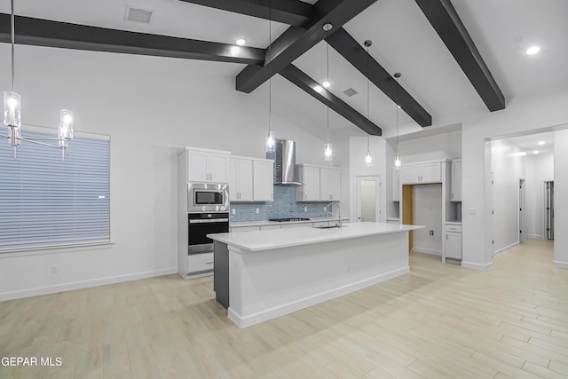 kitchen with white cabinets, wall chimney exhaust hood, pendant lighting, and appliances with stainless steel finishes