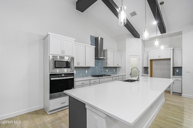 kitchen with a kitchen island with sink, wall chimney exhaust hood, high vaulted ceiling, and appliances with stainless steel finishes