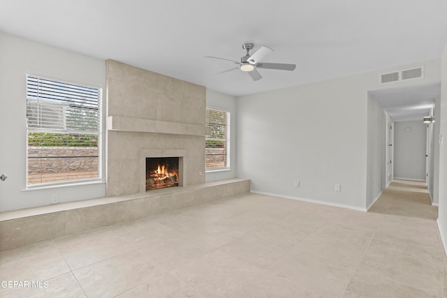 unfurnished living room with a fireplace, light tile patterned floors, a wealth of natural light, and ceiling fan