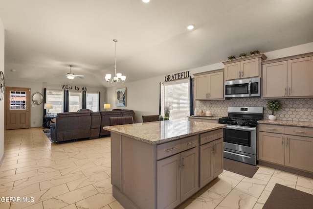 kitchen featuring a center island, appliances with stainless steel finishes, light stone counters, ceiling fan with notable chandelier, and tasteful backsplash