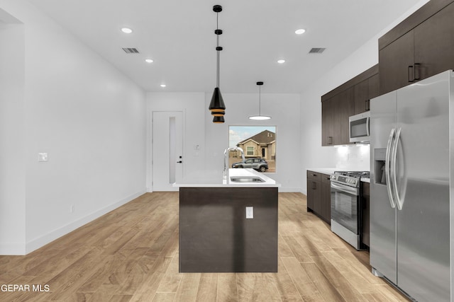 kitchen with appliances with stainless steel finishes, sink, an island with sink, and light hardwood / wood-style floors