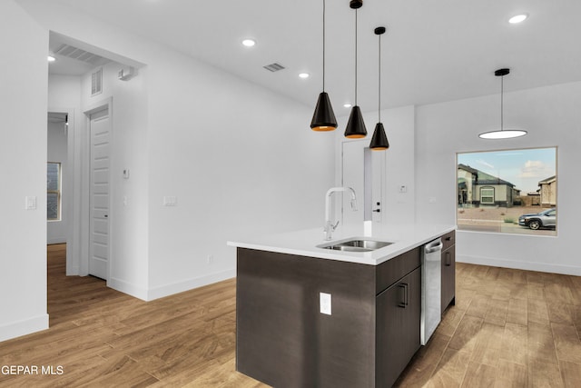 kitchen featuring a center island with sink, light wood-type flooring, hanging light fixtures, sink, and dark brown cabinetry