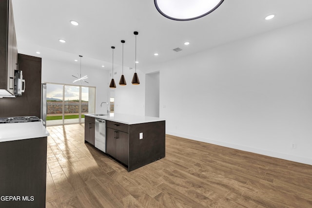 kitchen with appliances with stainless steel finishes, dark brown cabinets, hanging light fixtures, a center island with sink, and light wood-type flooring