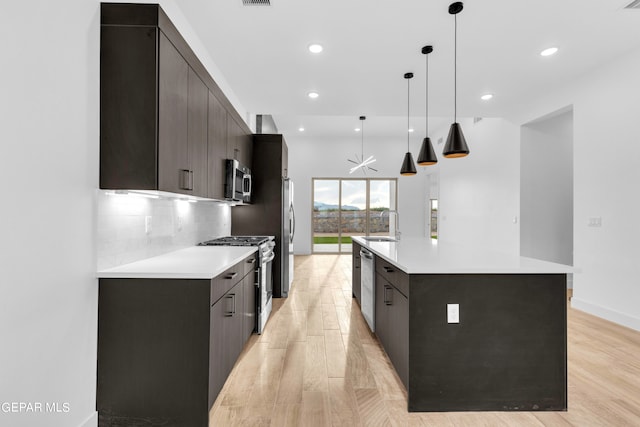 kitchen with pendant lighting, appliances with stainless steel finishes, a large island with sink, light hardwood / wood-style flooring, and decorative backsplash