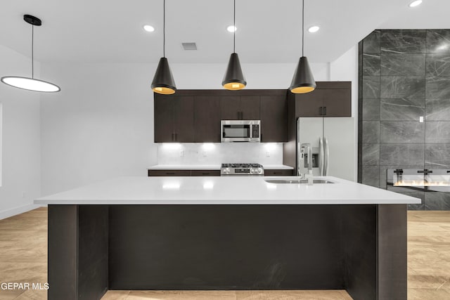 kitchen featuring appliances with stainless steel finishes, a center island with sink, light tile patterned floors, and hanging light fixtures