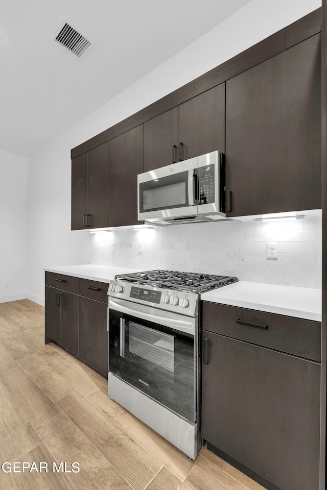 kitchen featuring appliances with stainless steel finishes, backsplash, light hardwood / wood-style flooring, and dark brown cabinets