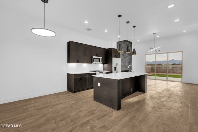 kitchen with appliances with stainless steel finishes, light hardwood / wood-style floors, a center island with sink, decorative light fixtures, and sink