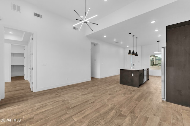 kitchen with a kitchen island with sink, light wood-type flooring, a raised ceiling, a chandelier, and decorative light fixtures