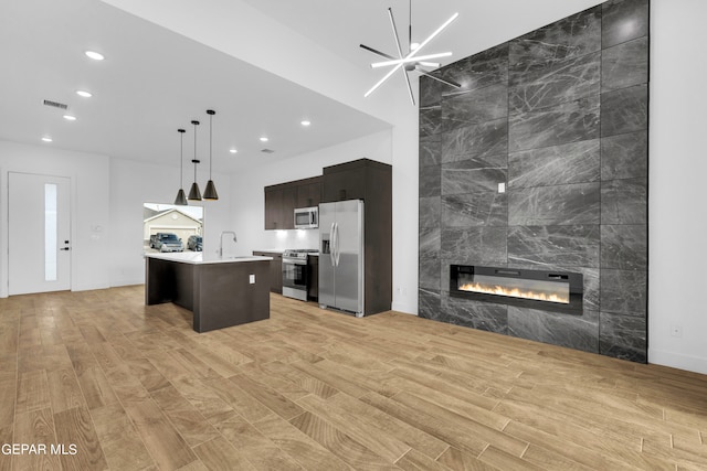 kitchen featuring a kitchen bar, appliances with stainless steel finishes, a kitchen island with sink, decorative light fixtures, and a tile fireplace