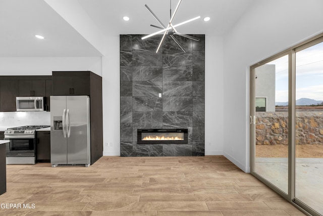 living room featuring a tile fireplace, tile walls, a notable chandelier, and light hardwood / wood-style floors