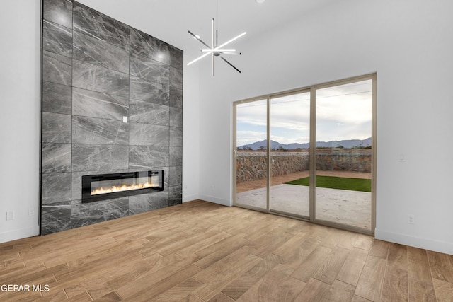 unfurnished living room with a notable chandelier, a mountain view, a tiled fireplace, tile walls, and light hardwood / wood-style flooring