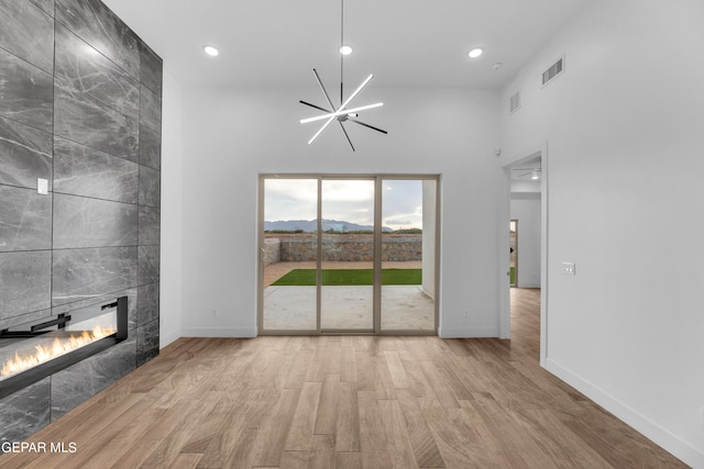 unfurnished living room with a towering ceiling, light hardwood / wood-style flooring, a tile fireplace, and a notable chandelier