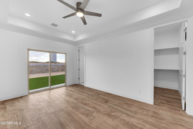 spare room with ceiling fan, a raised ceiling, and light wood-type flooring