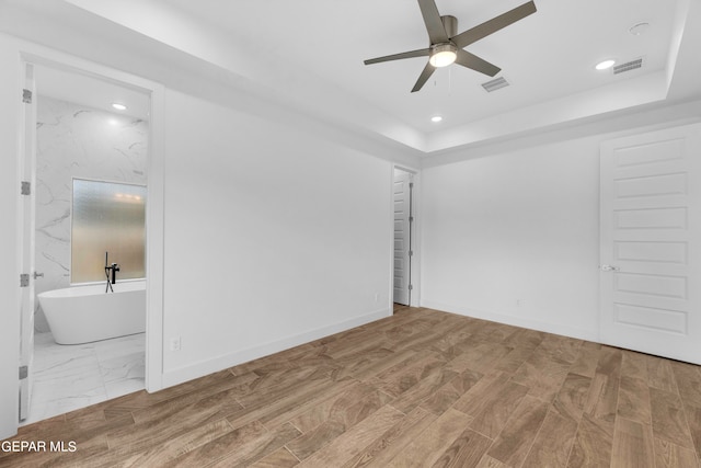 unfurnished bedroom featuring ceiling fan, a raised ceiling, hardwood / wood-style flooring, and ensuite bathroom