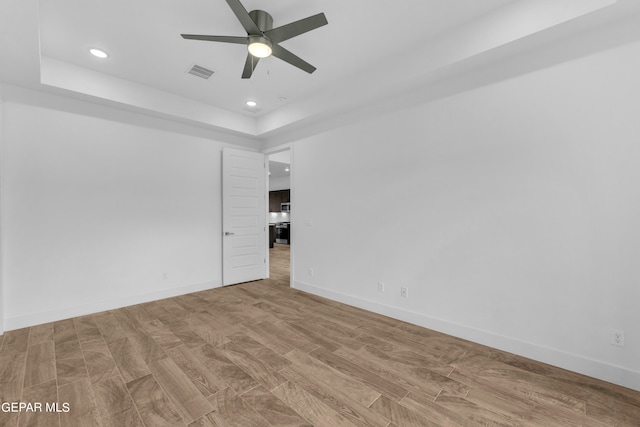 unfurnished room with a raised ceiling, ceiling fan, and light hardwood / wood-style floors