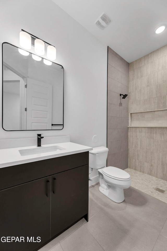 bathroom with toilet, a tile shower, vanity, and tile patterned flooring