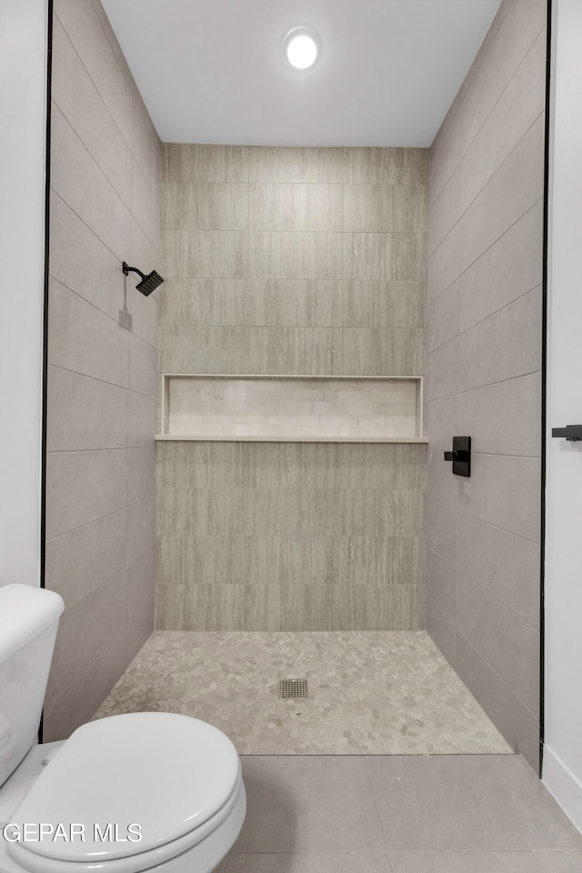 bathroom featuring toilet, a tile shower, and tile patterned flooring