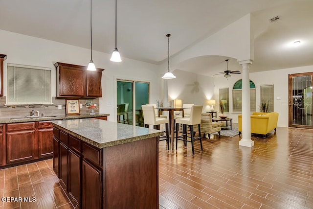 kitchen with light stone counters, ceiling fan, decorative backsplash, and ornate columns