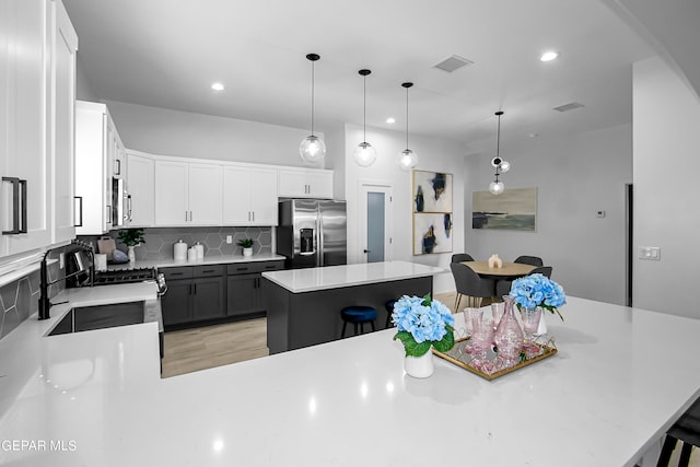 kitchen featuring white cabinets, a kitchen island, backsplash, appliances with stainless steel finishes, and a kitchen bar