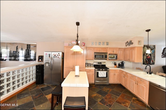 kitchen featuring stainless steel appliances, a sink, a kitchen island, light countertops, and stone tile flooring