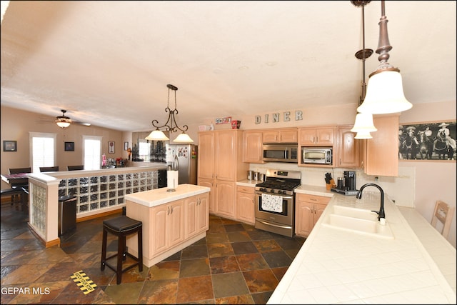 kitchen featuring sink, appliances with stainless steel finishes, dark tile patterned floors, a kitchen island, and light brown cabinets