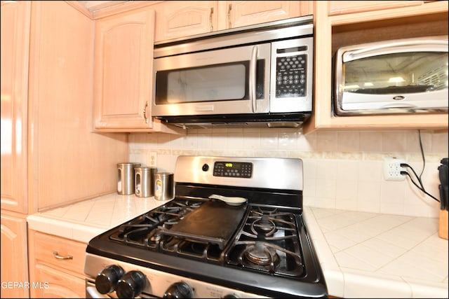 kitchen with tasteful backsplash, light brown cabinets, appliances with stainless steel finishes, and tile counters