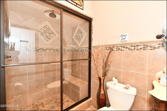 bathroom with toilet, a stall shower, tile walls, and wainscoting