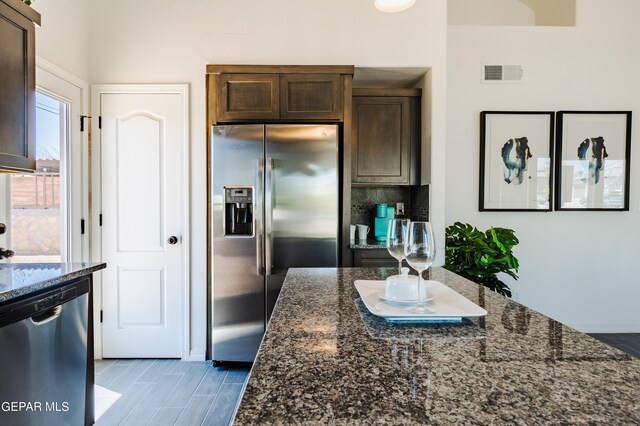 kitchen featuring dark stone counters, light hardwood / wood-style floors, dark brown cabinetry, and stainless steel appliances