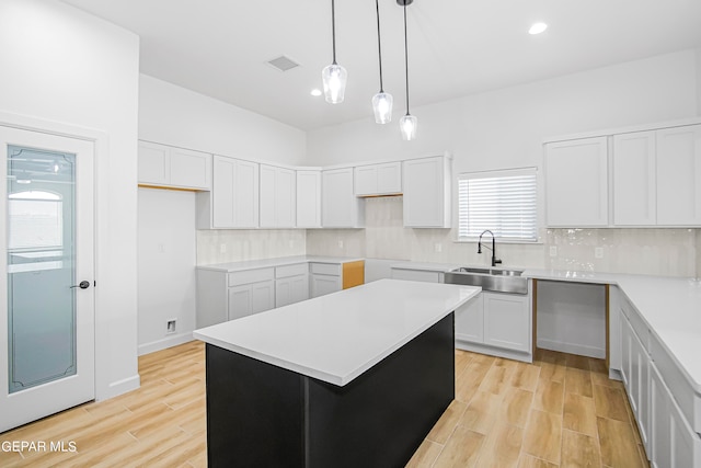 kitchen with light wood-type flooring, a kitchen island, sink, and white cabinetry