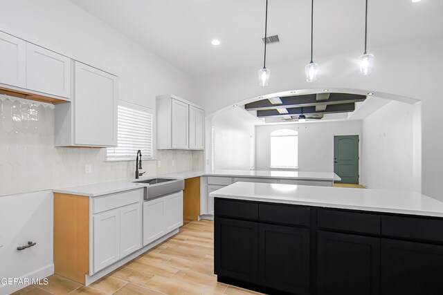 kitchen featuring white cabinets, pendant lighting, sink, tasteful backsplash, and light hardwood / wood-style floors