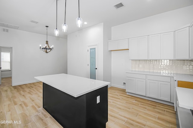 kitchen featuring light wood-type flooring, a center island, white cabinets, decorative backsplash, and decorative light fixtures