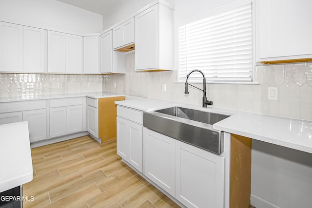 kitchen featuring light hardwood / wood-style flooring, backsplash, sink, and white cabinetry