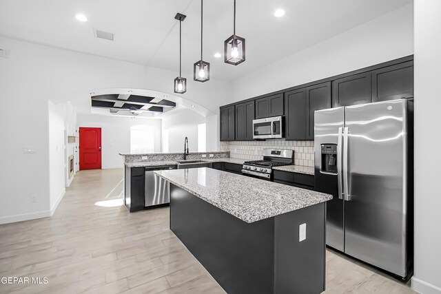 kitchen with decorative light fixtures, stainless steel appliances, sink, and a center island