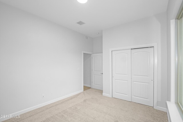 unfurnished bedroom with light colored carpet and a closet