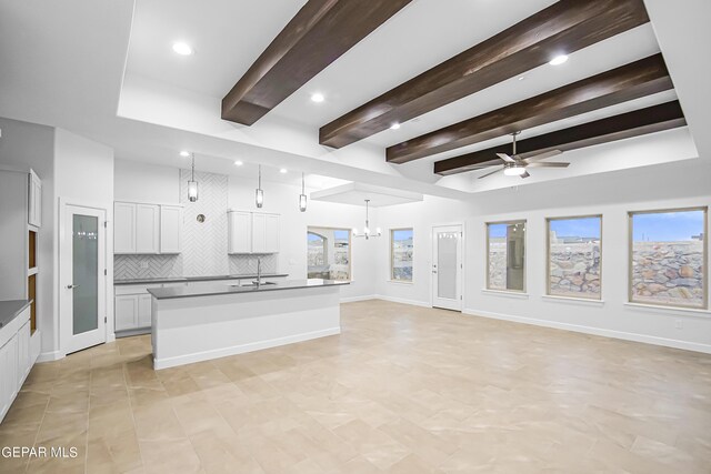 kitchen with an island with sink, tasteful backsplash, white cabinets, ceiling fan with notable chandelier, and decorative light fixtures