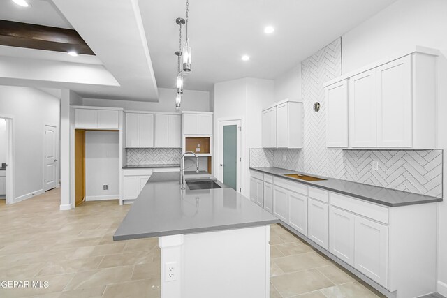 kitchen featuring white cabinets, an island with sink, hanging light fixtures, sink, and decorative backsplash