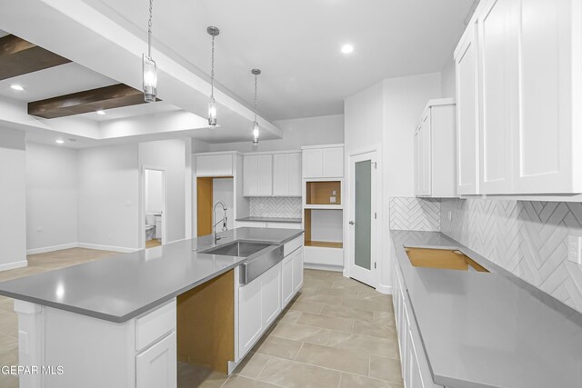 kitchen with beamed ceiling, sink, a center island with sink, backsplash, and white cabinetry