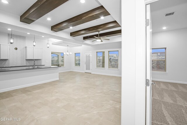 unfurnished living room with beamed ceiling, ceiling fan with notable chandelier, and sink