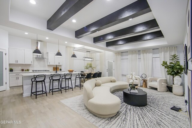 living room featuring light wood-type flooring, beam ceiling, and a raised ceiling