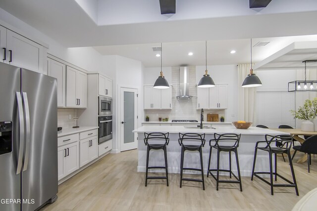 kitchen featuring decorative light fixtures, a kitchen island with sink, wall chimney range hood, stainless steel appliances, and decorative backsplash