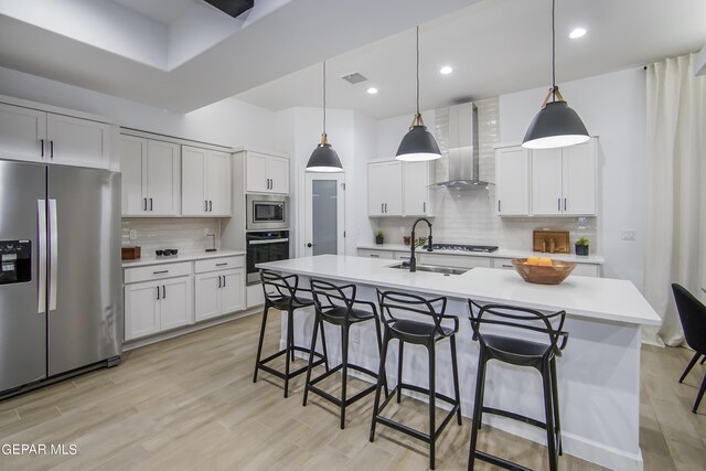 kitchen with pendant lighting, appliances with stainless steel finishes, white cabinets, and wall chimney range hood