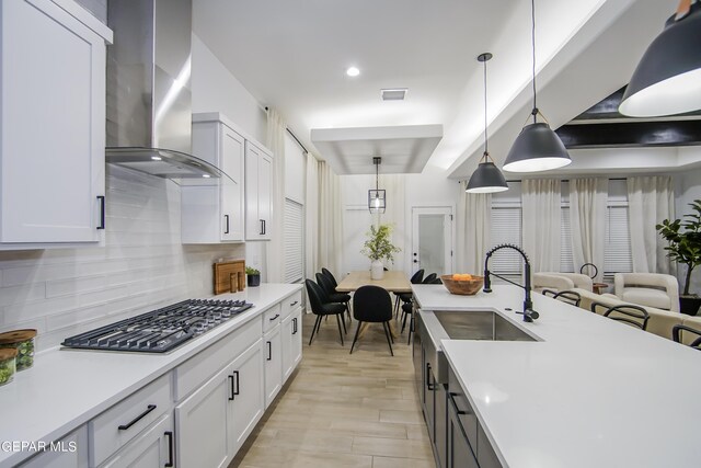 kitchen featuring wall chimney exhaust hood, stainless steel gas cooktop, pendant lighting, and white cabinetry