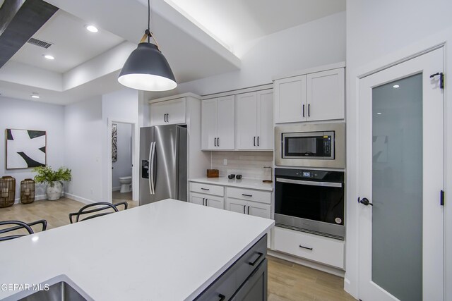 kitchen featuring a breakfast bar, white cabinets, stainless steel appliances, light wood-type flooring, and decorative light fixtures