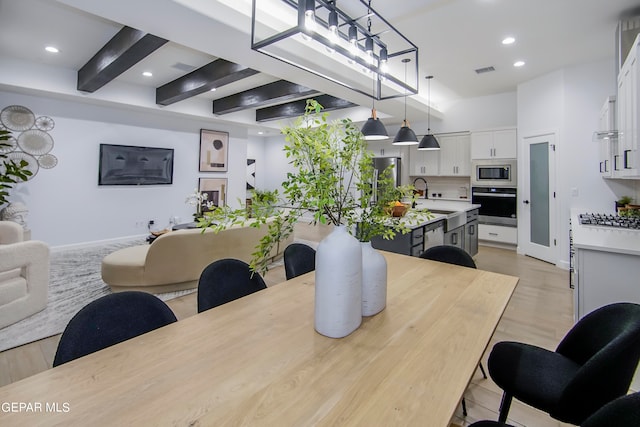 dining area with a notable chandelier, beamed ceiling, light wood-type flooring, and sink