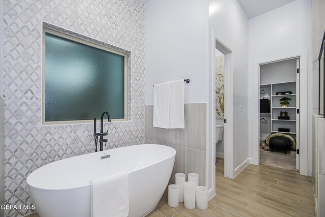 bathroom featuring hardwood / wood-style flooring, a tub to relax in, toilet, and tile walls