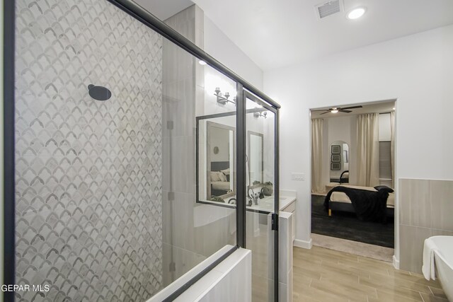 bathroom with ceiling fan, tile walls, a shower with shower door, and wood-type flooring