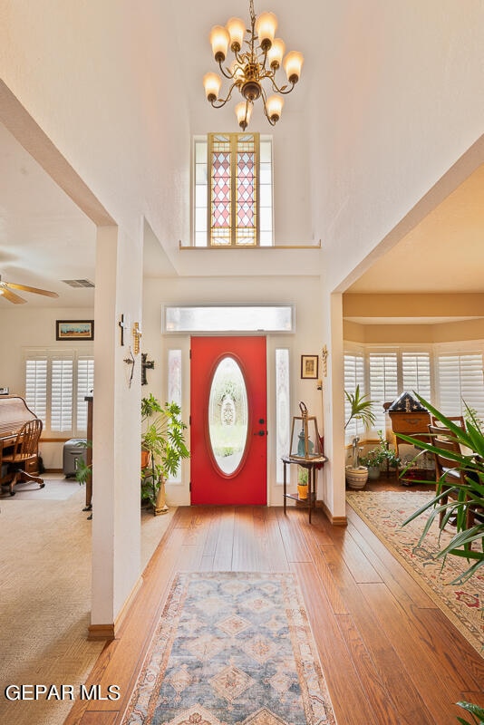 entryway featuring wood-type flooring, ceiling fan with notable chandelier, and a towering ceiling