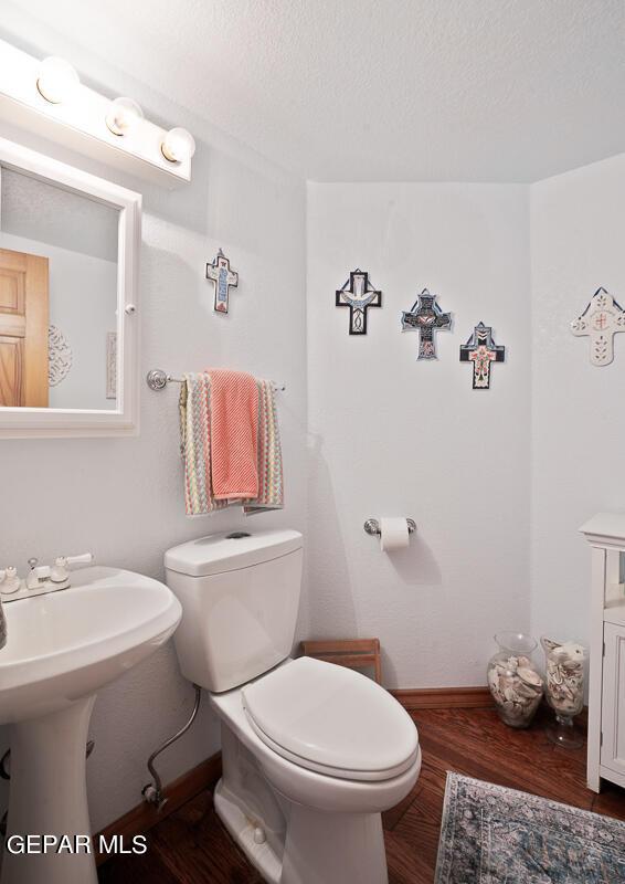 half bath with toilet, a sink, a textured ceiling, wood finished floors, and baseboards